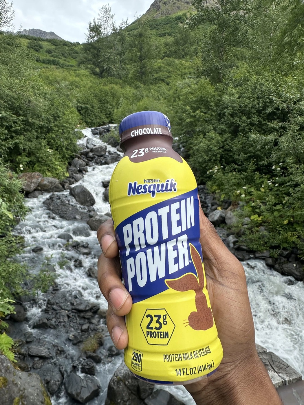 Nesquik Protein Power bottle held up in front of a mountain stream
